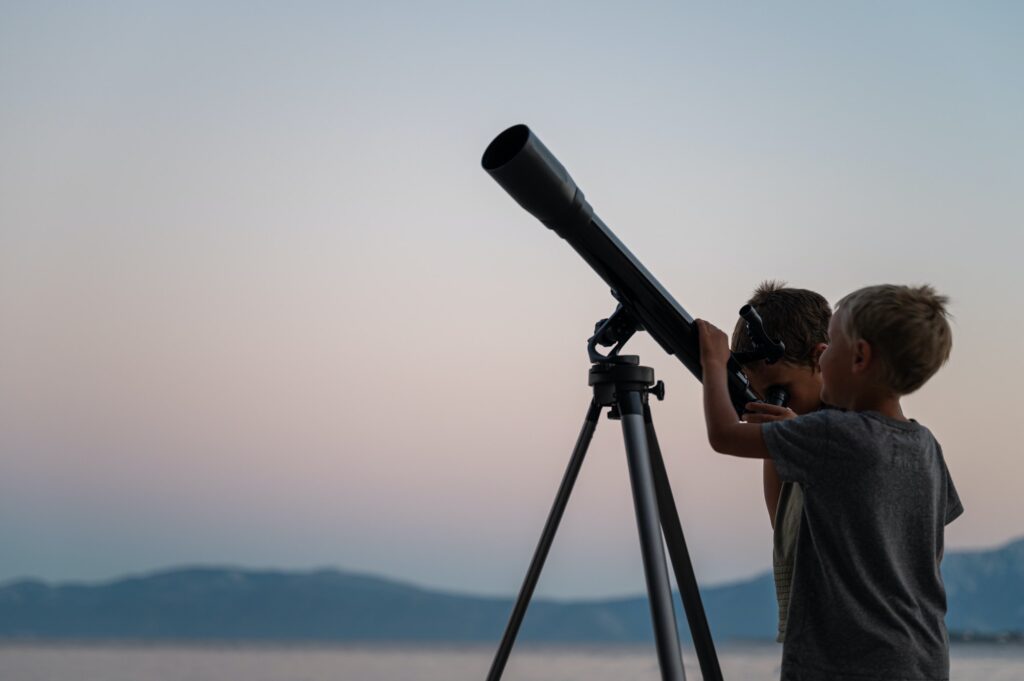 Two brothers looking at the stars using a telescope by the sea