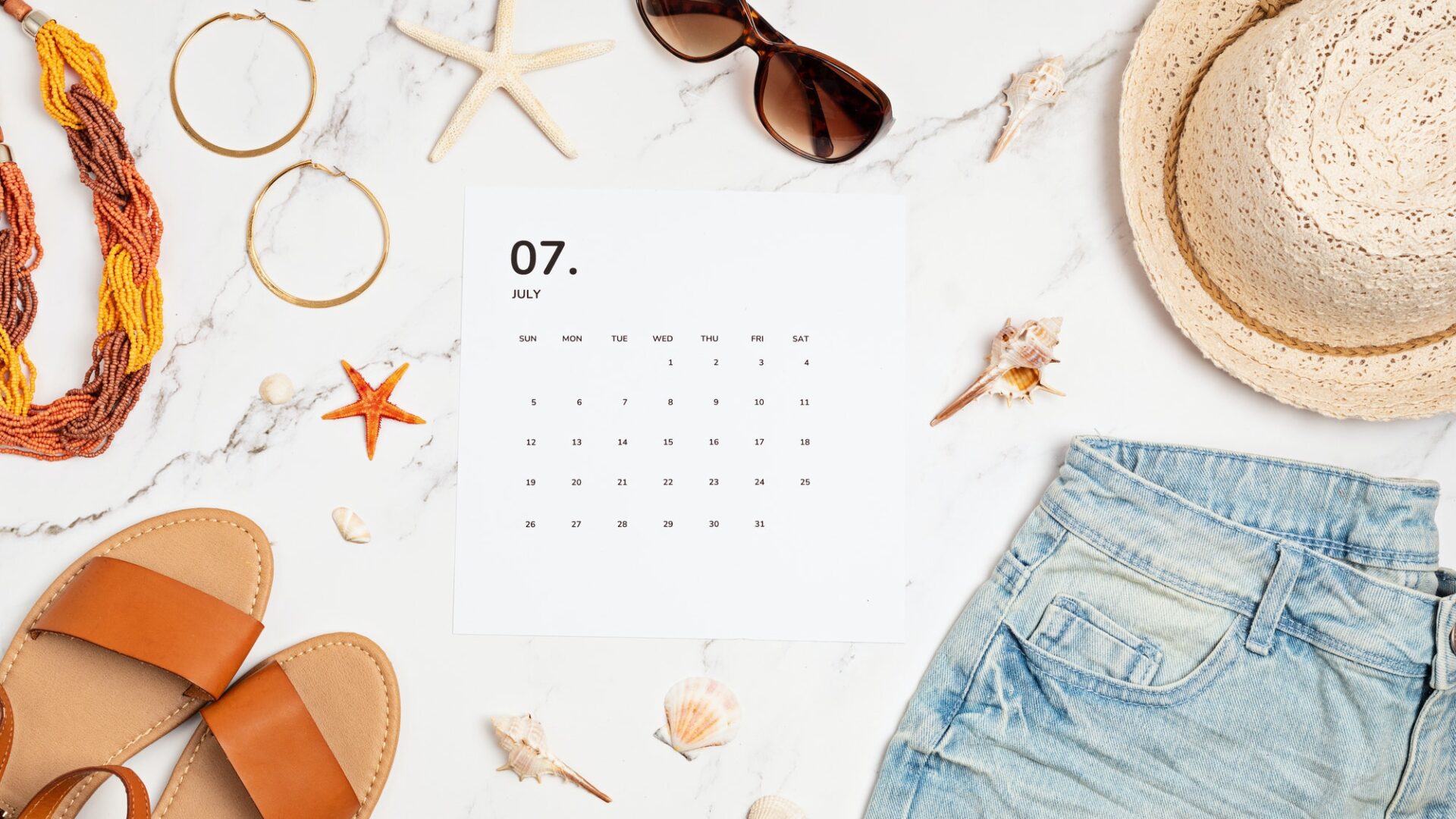 Flat lay with calendar for July with summer holidays fashion accessories