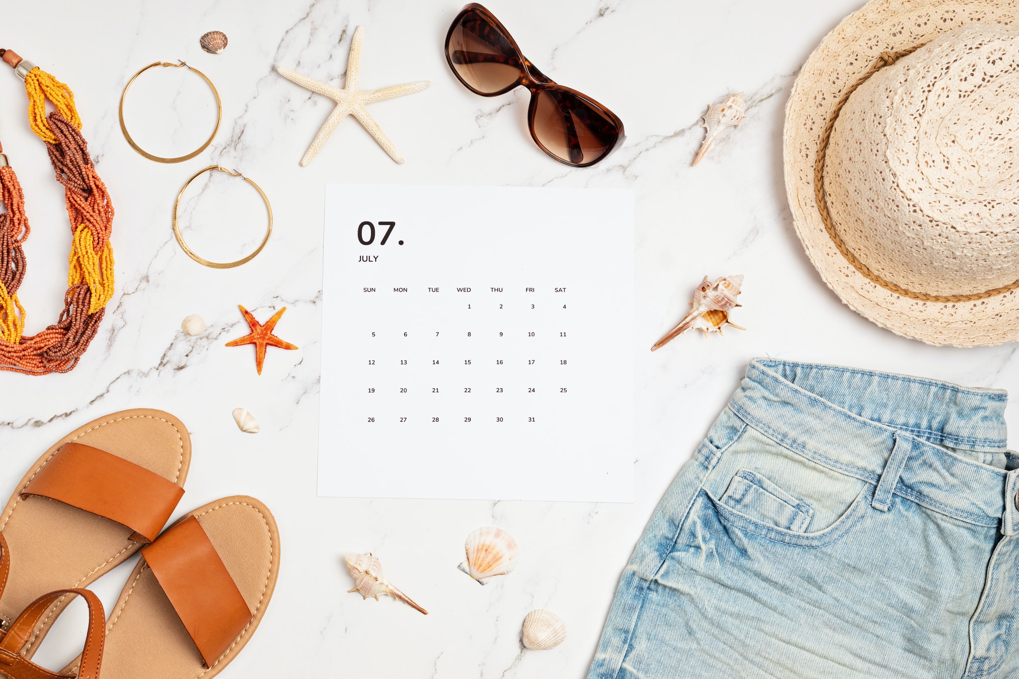 Flat lay with calendar for July with summer holidays fashion accessories