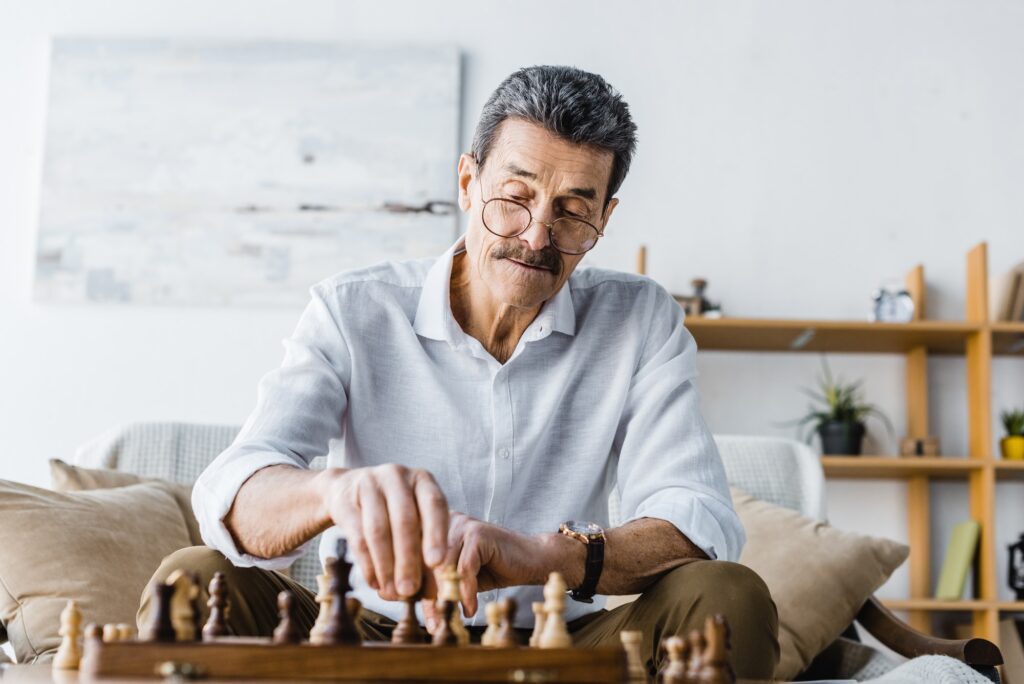 pensive senior man with mustache playing chess at home