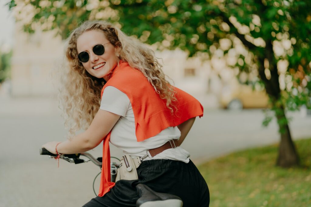 Delighted woman poses back at camera, rides bicycle outdoor