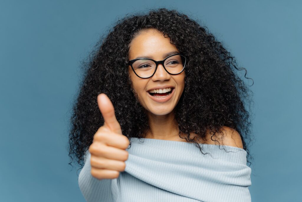 happy woman with Afro hairstyle, shows thumb up, gives positive opinion