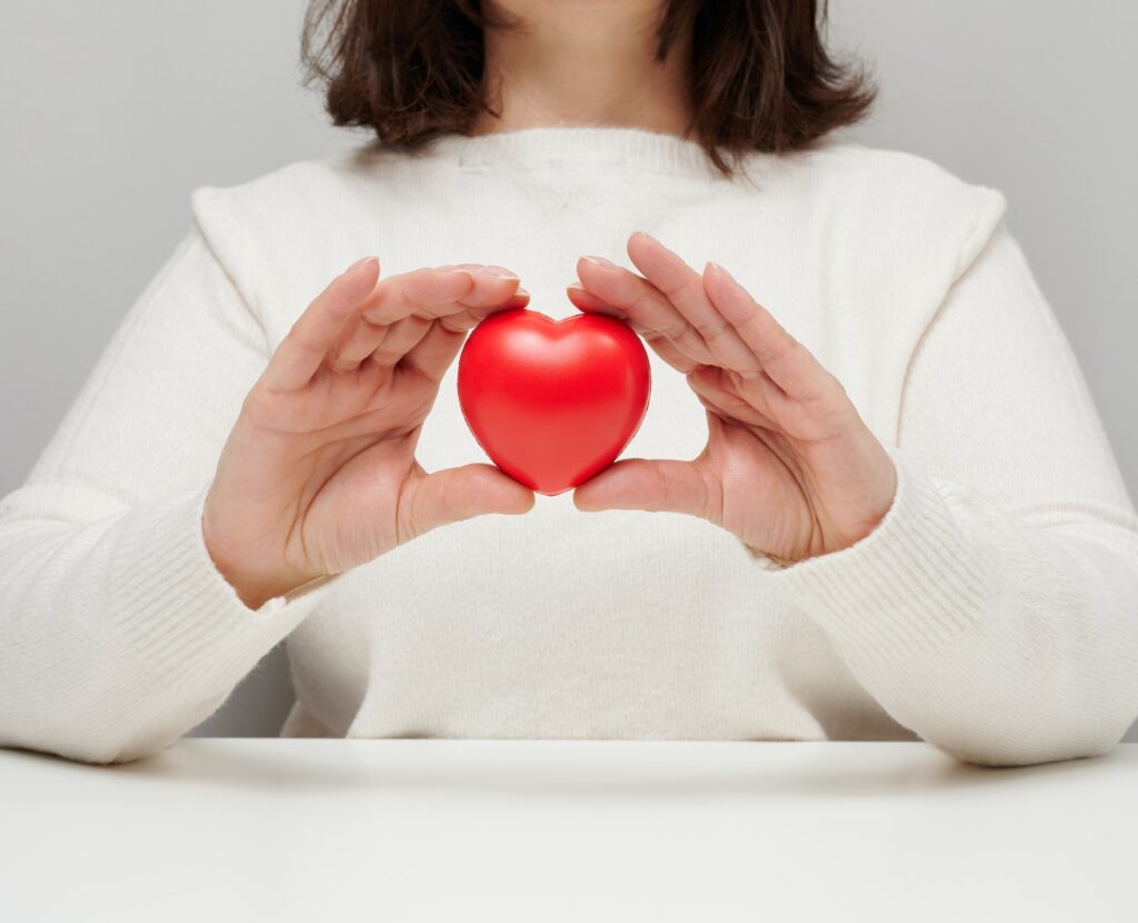 Woman in a white sweater holding a red heart, the concept of love and kindness. Donation