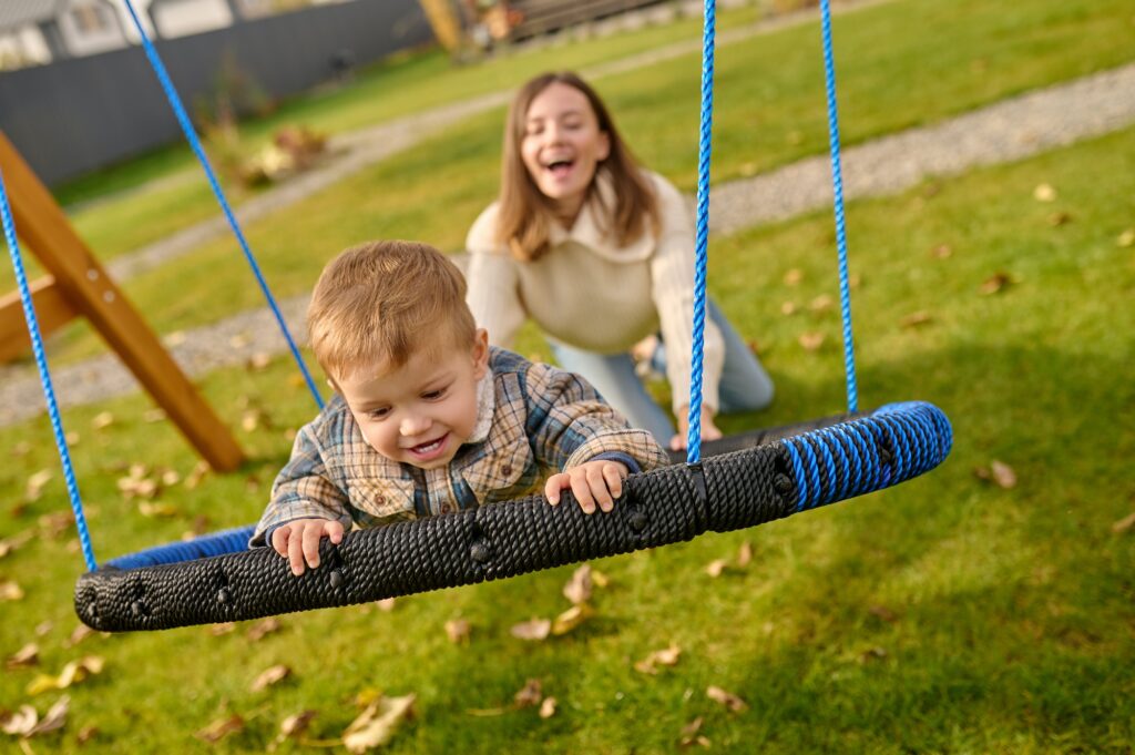 Woman pushing swing with joyful child
